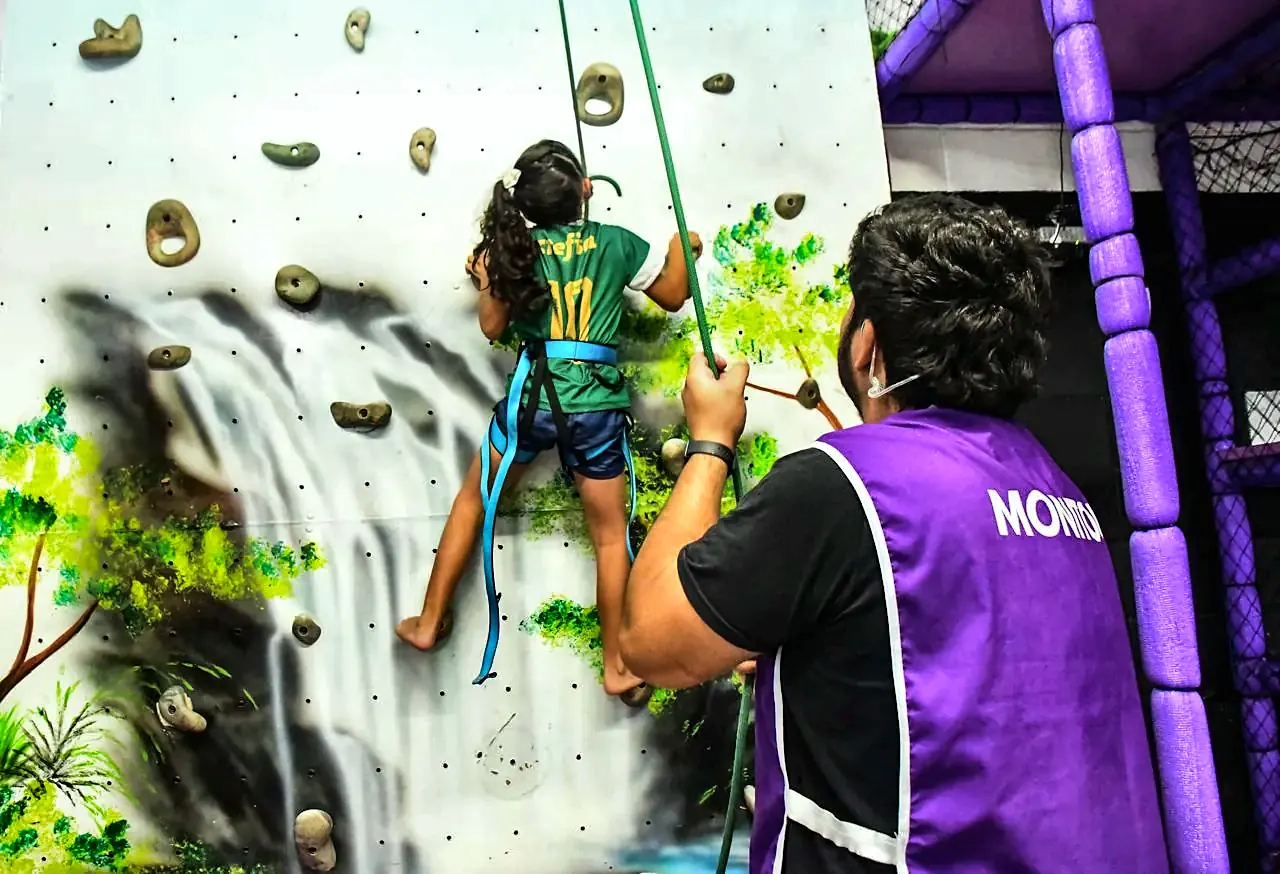 Criança na parede de escalada com monitor segurando a corda