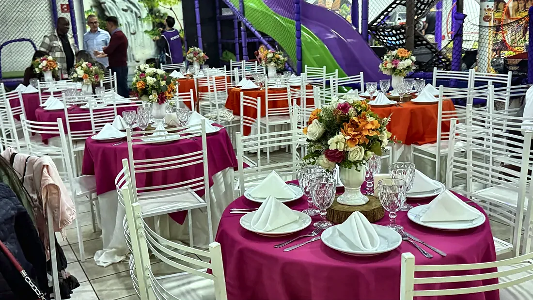 Mesas postas com toalhas em tom de rosa e arranjos de flores