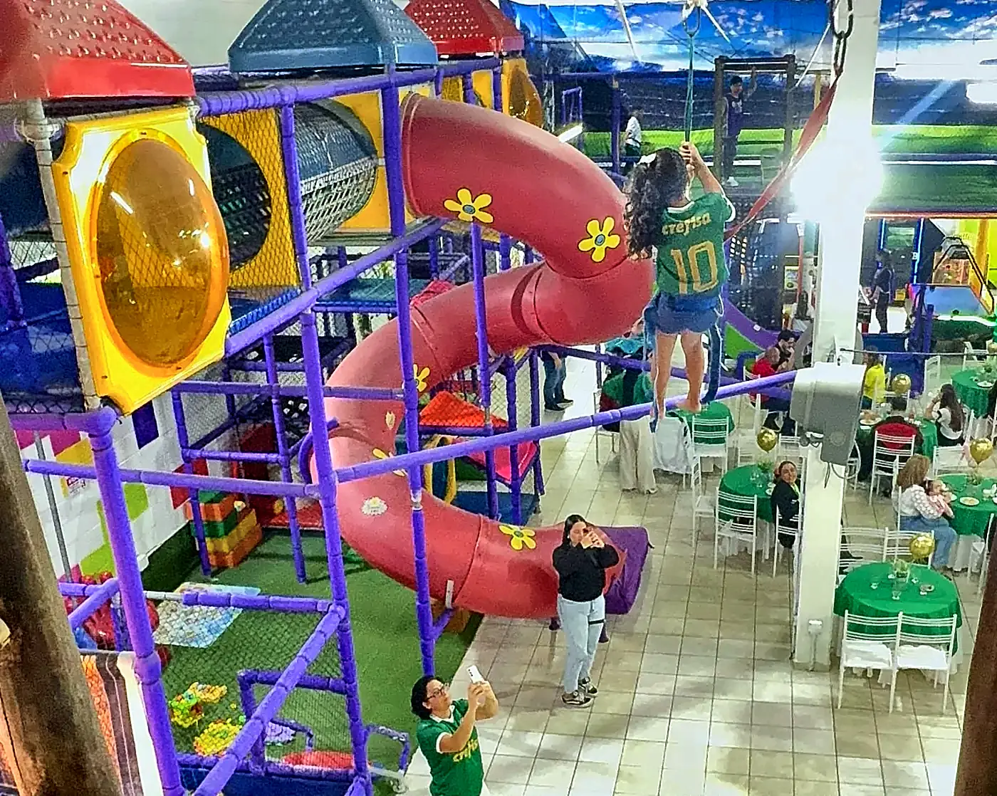 Criança de costas atravessando o salão na tirolesa, presa à cadeirinha de segurança